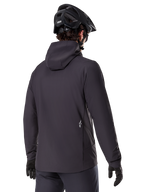 Veste thermique Alpinestars A-Dura, noire, vue de dos, portée avec un casque de VTT noir et des gants, avec un petit logo Astars blanc dans le bas du dos, veste de cyclisme légère et isolante