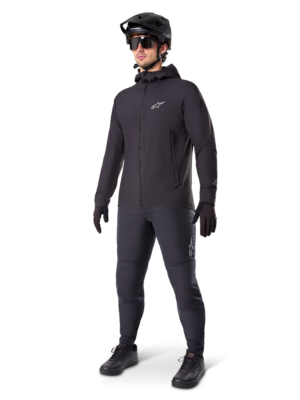 Veste thermique Alpinestars A-Dura en noir, portée par un cycliste avec un équipement complet de VTT incluant un casque noir, des lunettes de soleil et un pantalon de cyclisme, veste à capuche isolante et légère pour la performance à vélo par temps froid.
