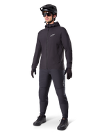 Veste thermique Alpinestars A-Dura en noir, portée par un cycliste avec un équipement complet de VTT incluant un casque noir, des lunettes de soleil et un pantalon de cyclisme, veste à capuche isolante et légère pour la performance à vélo par temps froid.