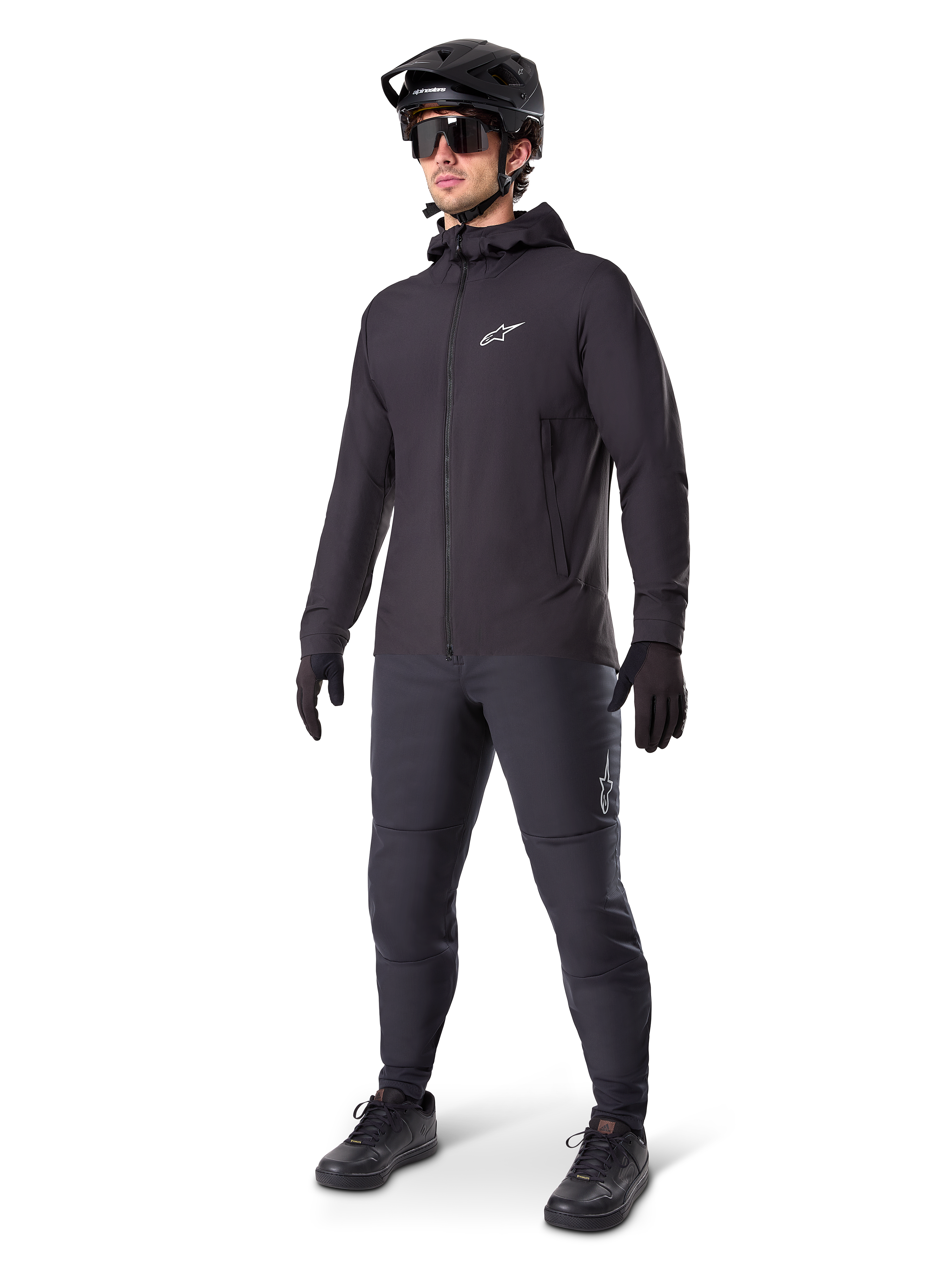 Veste thermique Alpinestars A-Dura en noir, portée par un cycliste avec un équipement complet de VTT incluant un casque noir, des lunettes de soleil et un pantalon de cyclisme, veste à capuche isolante et légère pour la performance à vélo par temps froid.