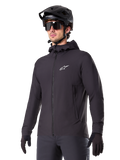 Veste thermique Alpinestars A-Dura, veste de cyclisme noire, modèle à capuche avec fermeture éclair frontale, logo étoile blanc sur la poitrine, portée avec casque de VTT et gants noirs, équipement de performance pour le VTT par temps froid