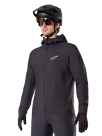 Veste thermique Alpinestars A-Dura, veste de cyclisme noire, modèle à capuche avec fermeture éclair frontale, logo étoile blanc sur la poitrine, portée avec casque de VTT et gants noirs, équipement de performance pour le VTT par temps froid