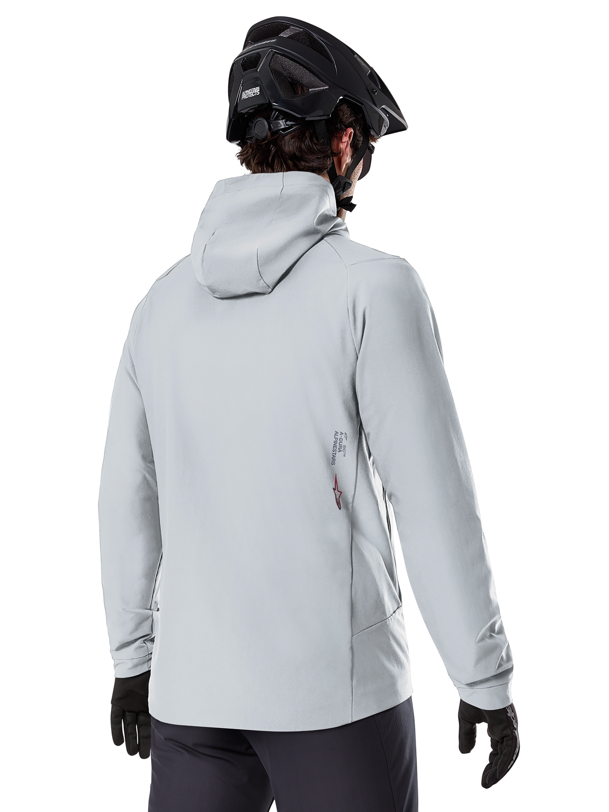 Alpinestars A-Dura Thermal Jacket, Titanium grijs, achteraanzicht van een rijder die de geïsoleerde jas met capuchon draagt, gecombineerd met een zwarte MTB-helm en zwarte handschoenen, met een klein Alpinestars-logo op de onderrug, ontworpen voor mountainbiken in koud weer