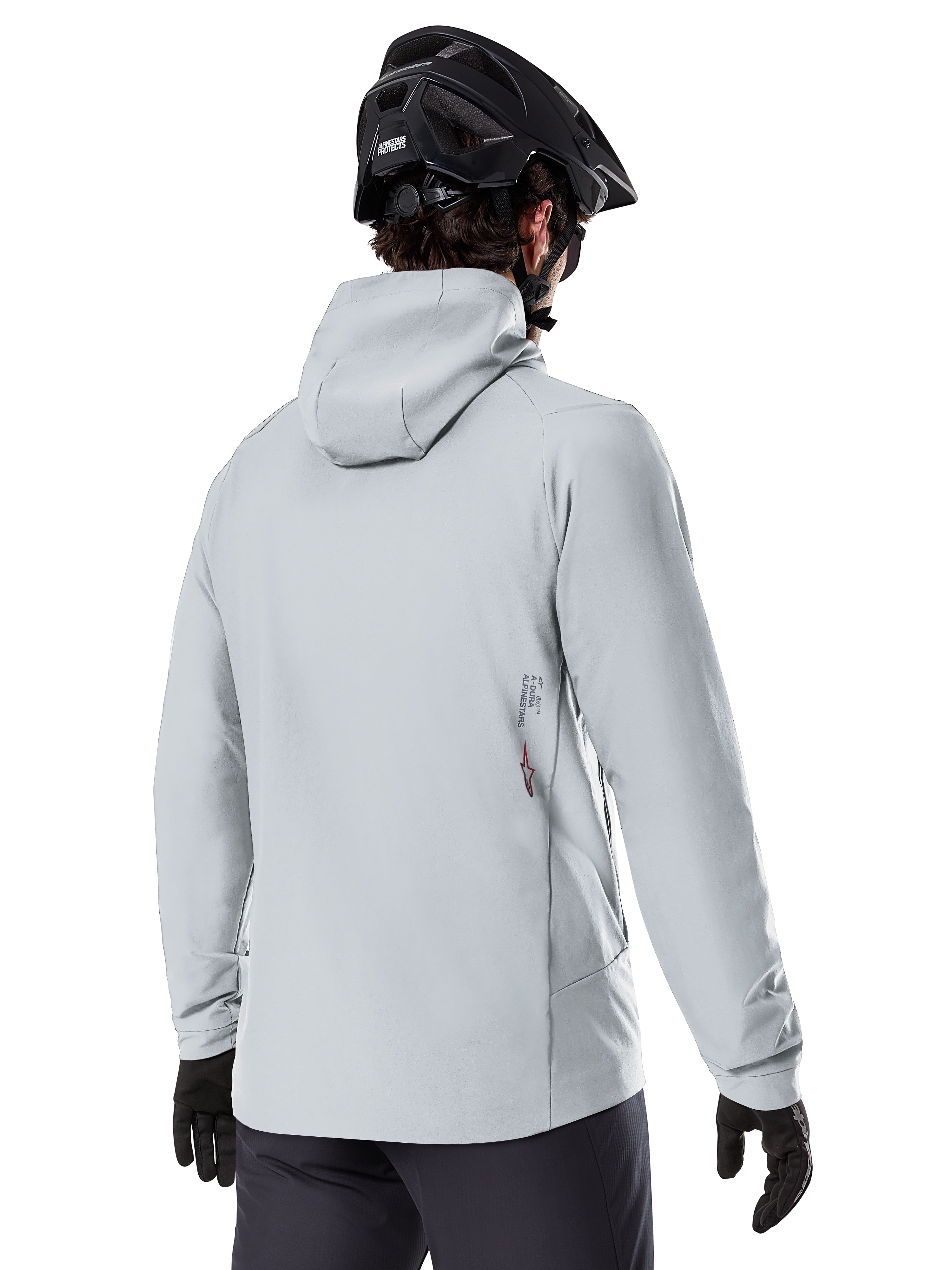 Alpinestars A-Dura Thermal Jacket, Titanium grijs, achteraanzicht van een rijder die de geïsoleerde jas met capuchon draagt, gecombineerd met een zwarte MTB-helm en zwarte handschoenen, met een klein Alpinestars-logo op de onderrug, ontworpen voor mountainbiken in koud weer