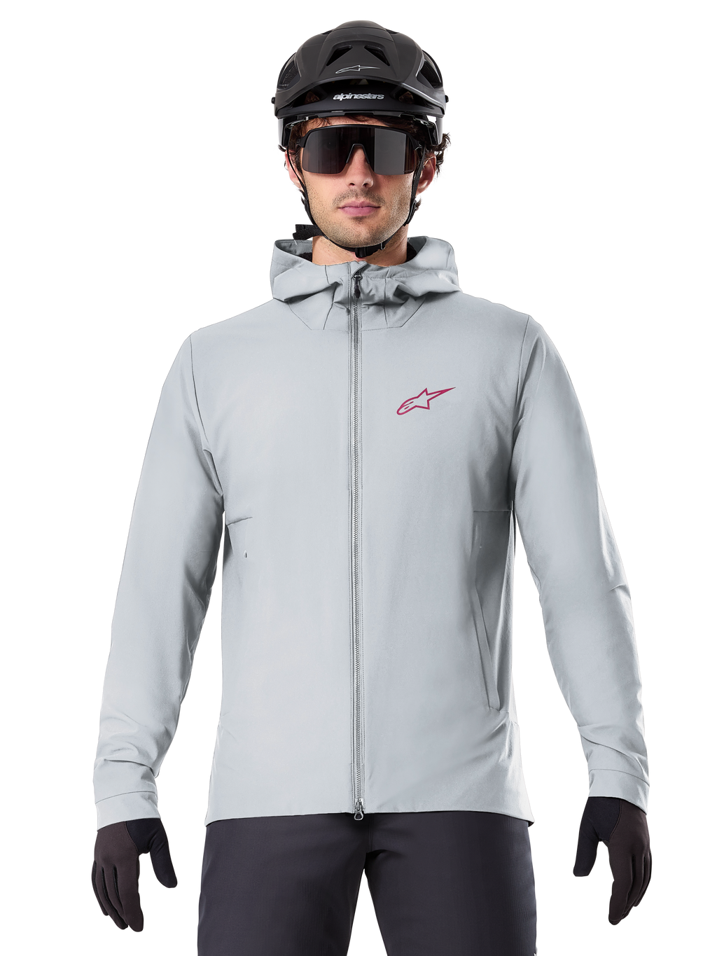 Alpinestars A-Dura Thermal Jacket in Titanium, lichtgrijze fietsjas met capuchon, rood sterlogo op de borst, gedragen door een rijder met zwarte MTB-helm, zonnebril en handschoenen, geïsoleerde kleding voor mountainbiken