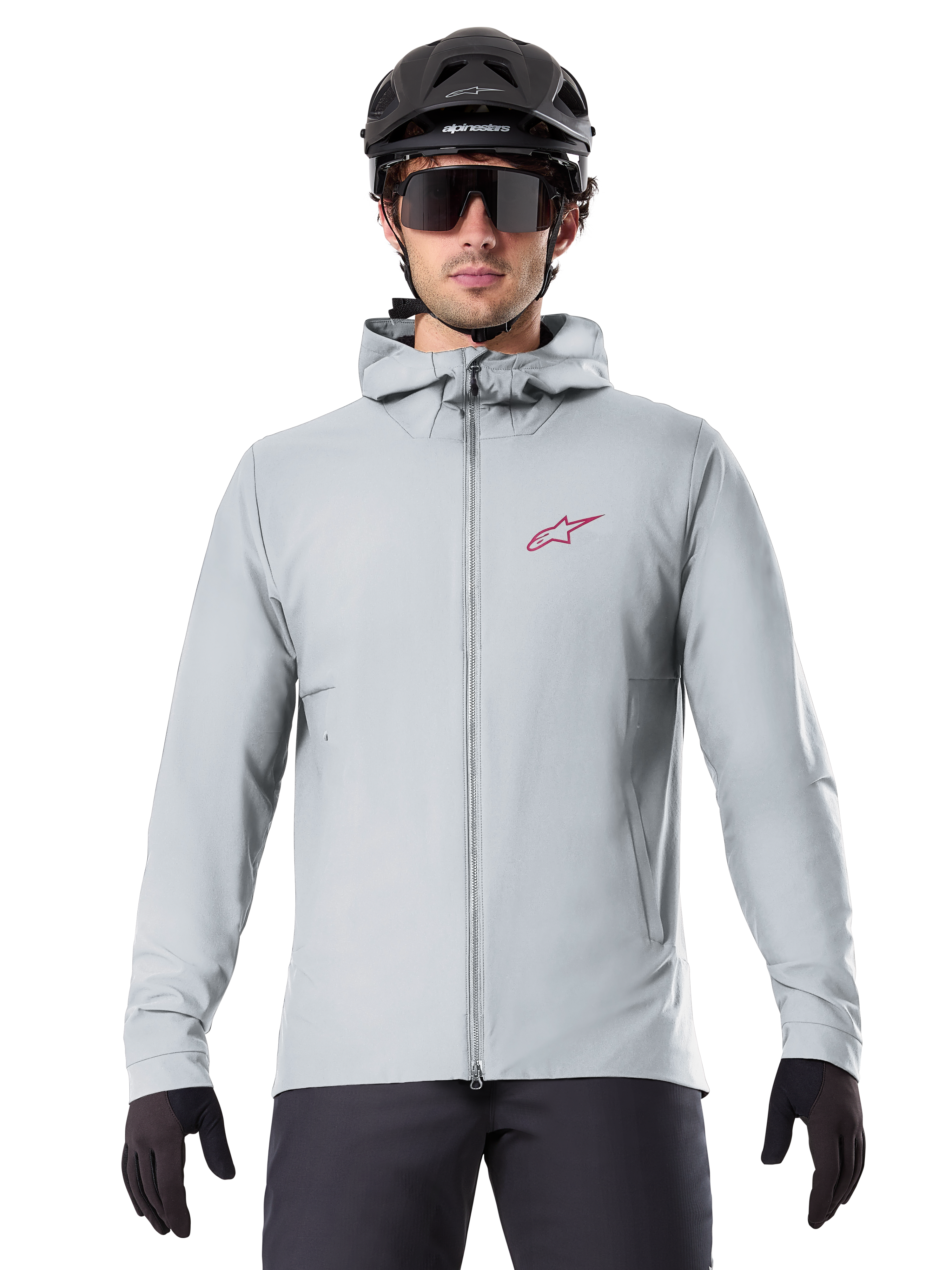 Alpinestars A-Dura Thermal Jacket in Titanium, lichtgrijze fietsjas met capuchon, rood sterlogo op de borst, gedragen door een rijder met zwarte MTB-helm, zonnebril en handschoenen, geïsoleerde kleding voor mountainbiken
