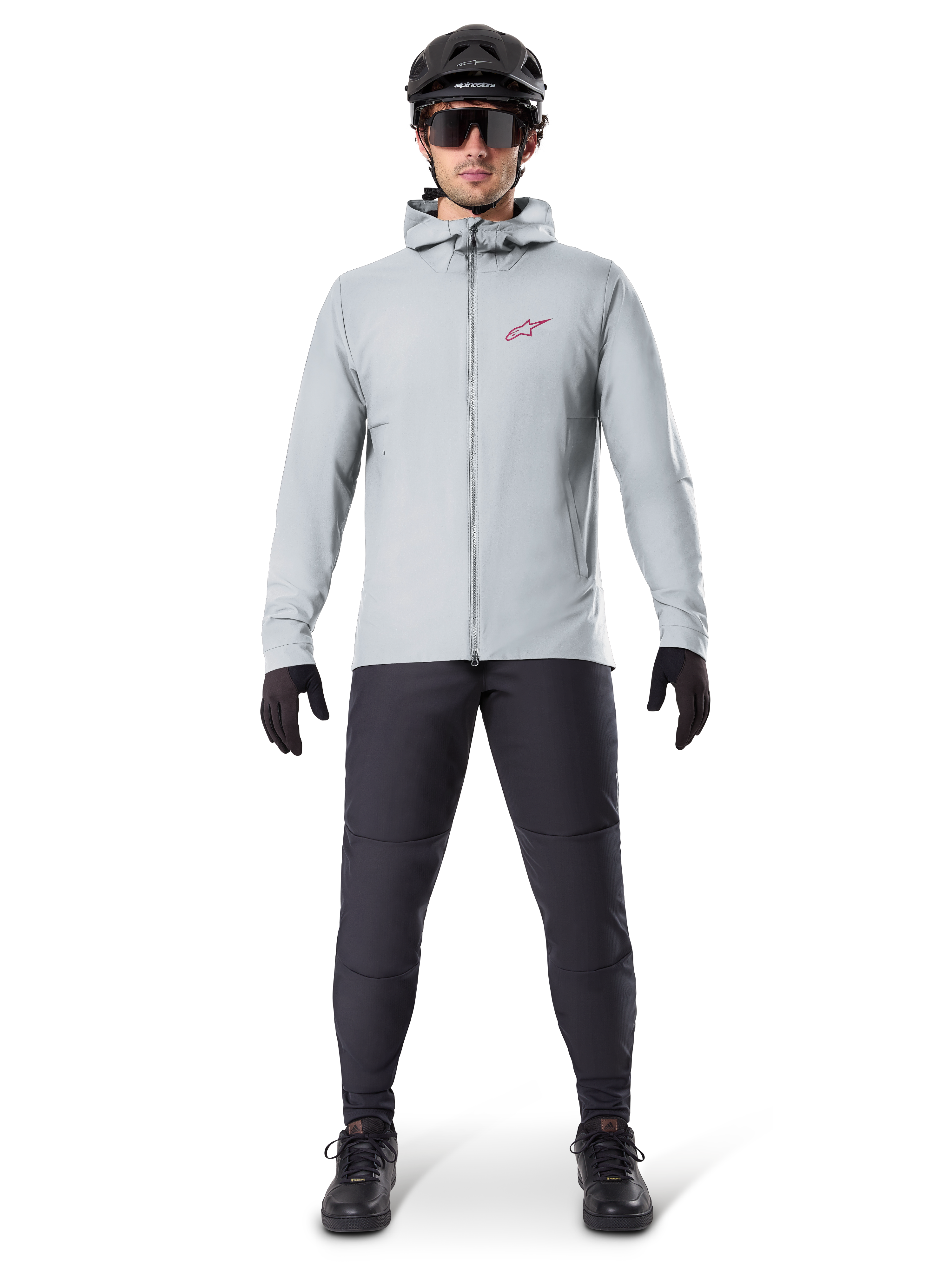 Alpinestars A-Dura Thermal Jacket, titanium grijs, fietsjas gedragen met zwarte mountainbikebroek, handschoenen en helm, voorzien van een klein rood sterlogo op de borst en een volledige ritssluiting aan de voorzijde, lichtgewicht geïsoleerde kleding voor off-road ritten