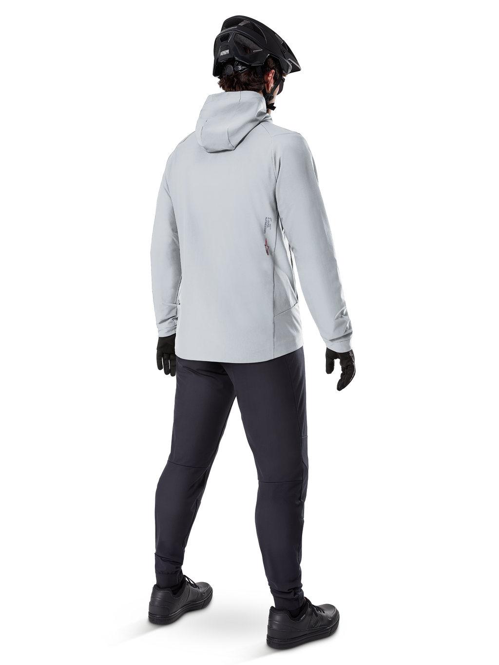 Alpinestars A-Dura Thermal Jacket in Titanium, achteraanzicht van mannelijke fietser die een lichtgrijze thermische jas met capuchon draagt, gecombineerd met zwarte MTB-helm, zwarte handschoenen en donkergrijze broek, functionele mountainbike-uitrusting
