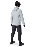 Alpinestars A-Dura Thermal Jacket in Titanium, achteraanzicht van mannelijke fietser die een lichtgrijze thermische jas met capuchon draagt, gecombineerd met zwarte MTB-helm, zwarte handschoenen en donkergrijze broek, functionele mountainbike-uitrusting