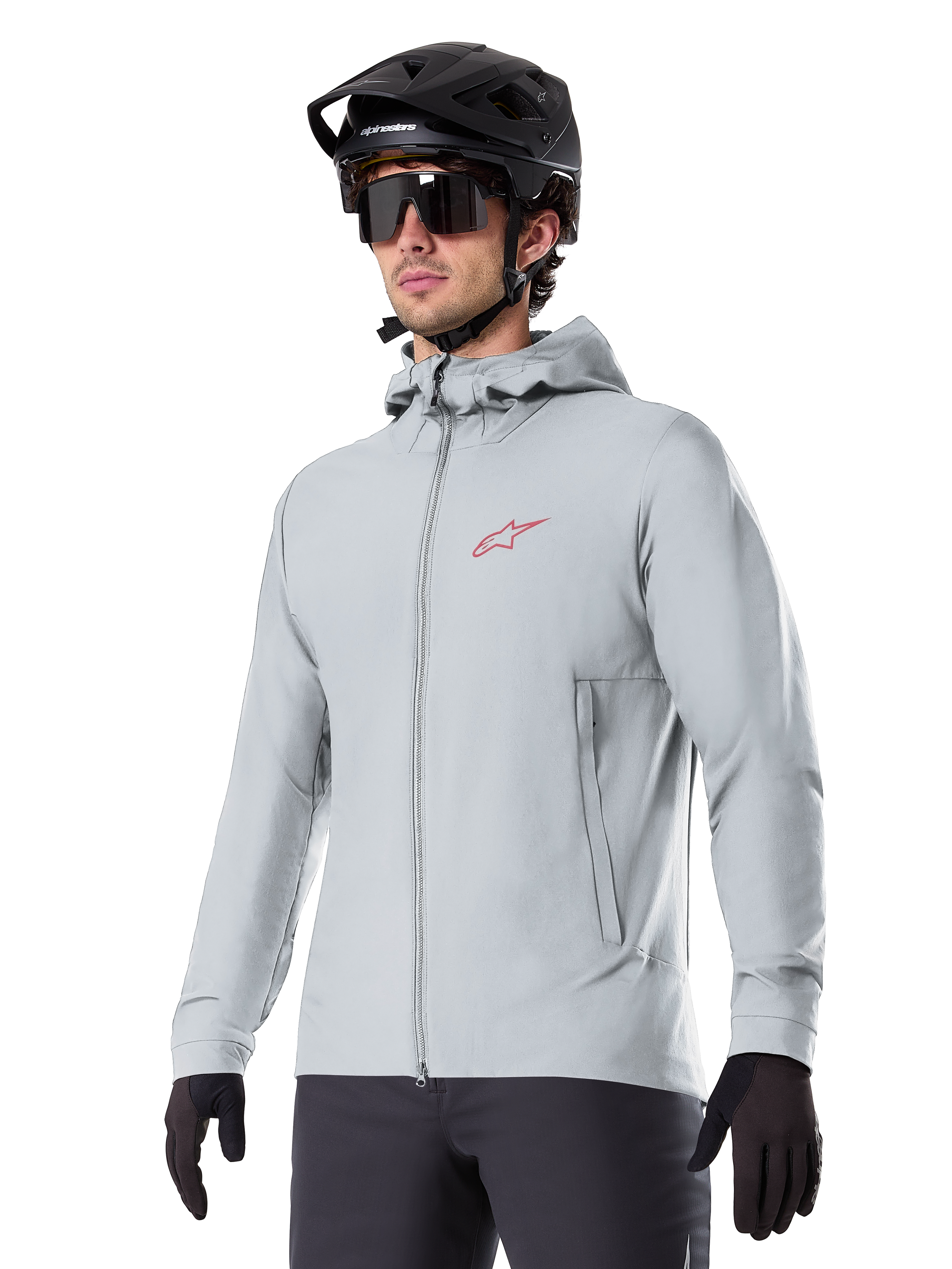 Alpinestars A-Dura Thermal Jacket, lichtgrijze geïsoleerde fietsjas, model met capuchon en een klein rood logo, gedragen met een zwarte helm en handschoenen, technische mountainbikekleding voor ritten in koud weer