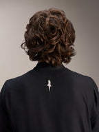 Veste coupe-vent Alpinestars A-Aria, noire, vue rapprochée de dos du haut des épaules et du col, avec un petit logo blanc au centre du dos, portée par un mannequin aux cheveux bruns ondulés, équipement de cyclisme technique et minimaliste