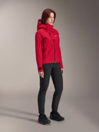 Alpinestars Stella A-Dura Elite waterdichte damesjas, Rood Fluo, mountainbike-regenjas met capuchon en wit Astars-logo op de borstflap, gedragen met zwarte broek en zwarte mountainbikeschoenen, technische prestatiekleding voor trailrijden