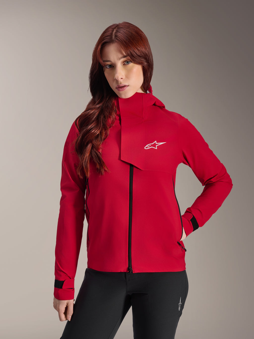 Alpinestars Stella A-Dura Elite Waterdichte Jas, mountainbikejas voor dames, Red Fluo, met een stormflap aan de voorzijde voorzien van een wit Alpinestars-logo, hoge kraag en verstelbare manchetten, gedragen met een zwarte broek voor een technische rijlook