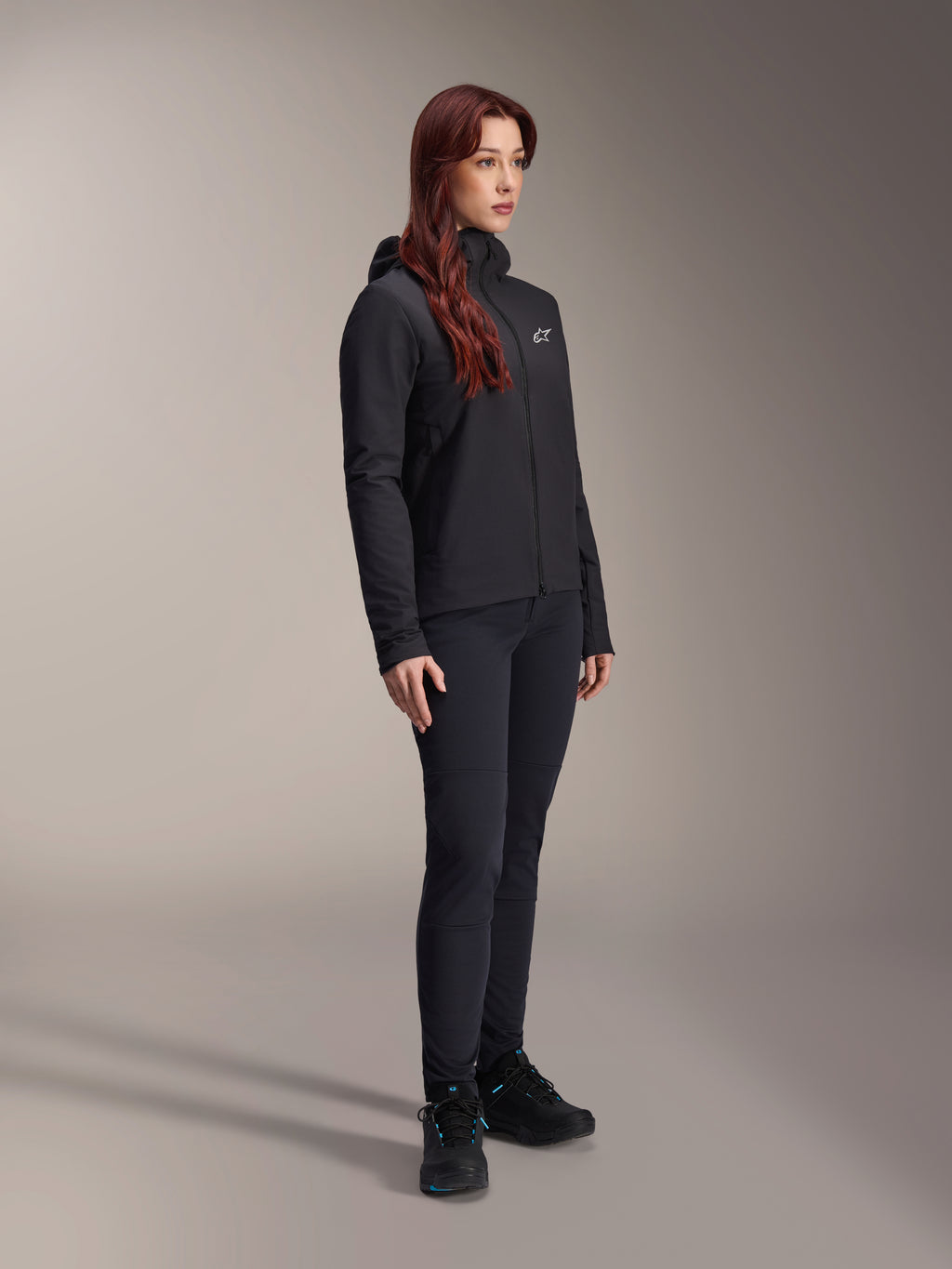 Alpinestars Stella A-Dura Thermojas, zwarte lichtgewicht geïsoleerde damesjas met capuchon, gedragen met een zwarte broek en zwarte schoenen, professionele wielren- en mountainbike-outfit voor koude omstandigheden