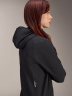 Alpinestars Stella A-Dura Thermal Jacket, dames fietsjack, zwart, zijprofiel van een vrouw met rood haar die de jas draagt, voorzien van een geïntegreerde capuchon en wit Alpinestars sterlogo aan de zijkant, lichtgewicht geïsoleerde thermische kleding voor MTB