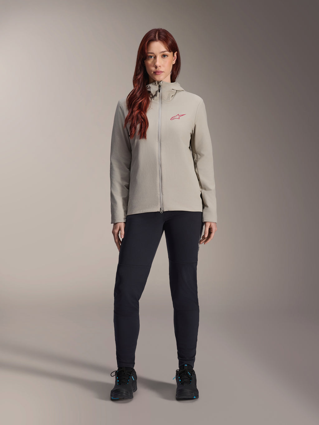 Veste thermique Alpinestars Stella A-Dura pour femme, veste de VTT, gris titane, portée avec un pantalon technique noir et des chaussures noires, dotée d'une capuche doublée de polaire et d'un logo rouge sur la poitrine, conçue pour les sorties par temps froid