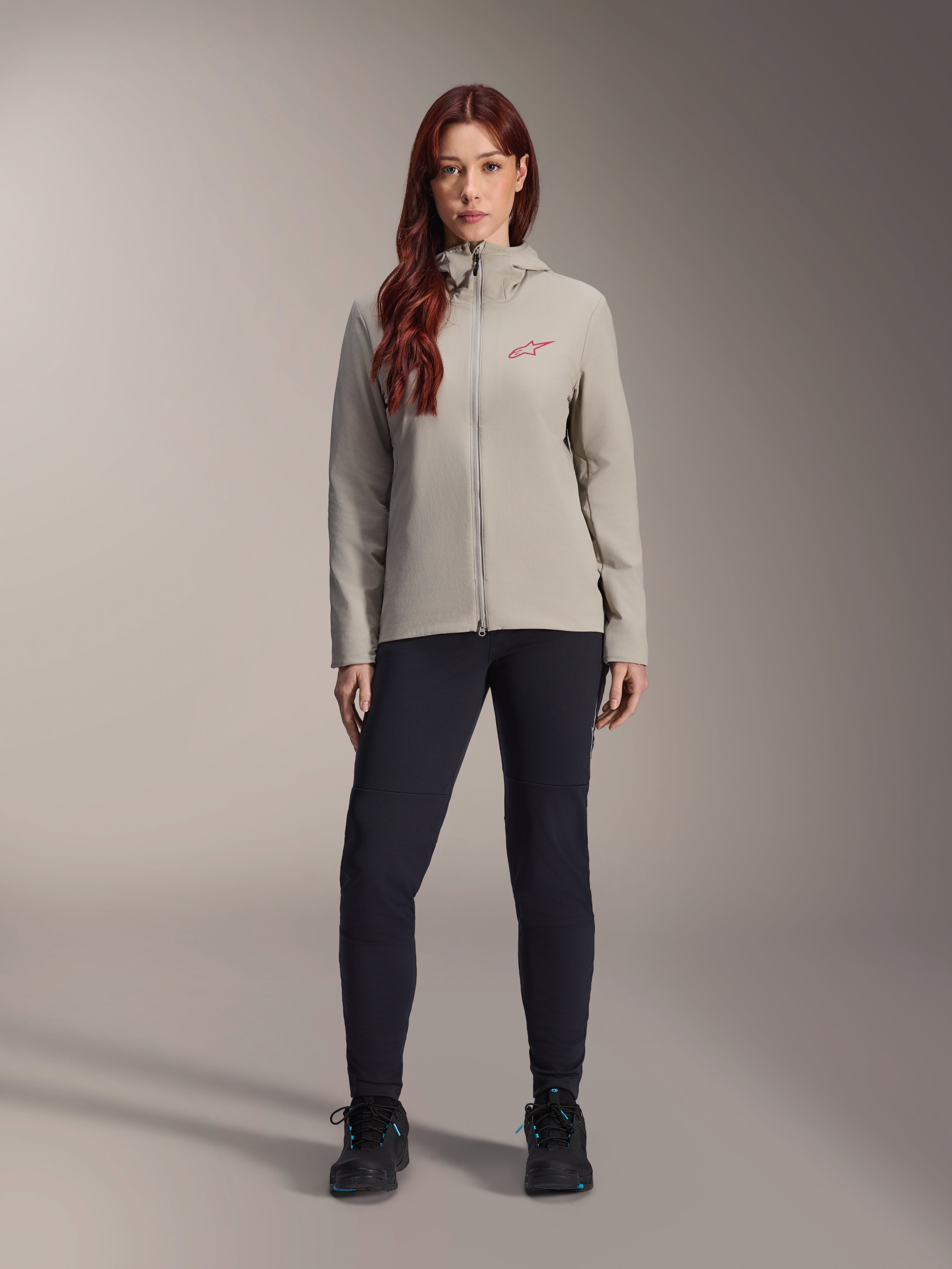 Veste thermique Alpinestars Stella A-Dura pour femme, veste de VTT, gris titane, portée avec un pantalon technique noir et des chaussures noires, dotée d'une capuche doublée de polaire et d'un logo rouge sur la poitrine, conçue pour les sorties par temps froid