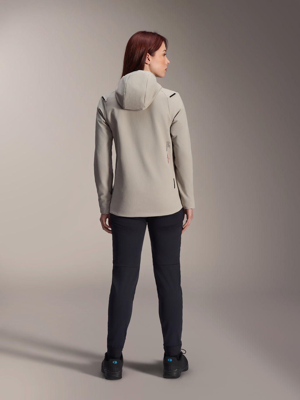 Veste thermique femme Alpinestars Stella A-Dura, Gris Titane, vue de dos portée avec un pantalon noir, dotée d'une capuche isolée doublée de polaire et d'un petit logo rouge, veste de VTT fonctionnelle et élégante pour rouler par temps froid.