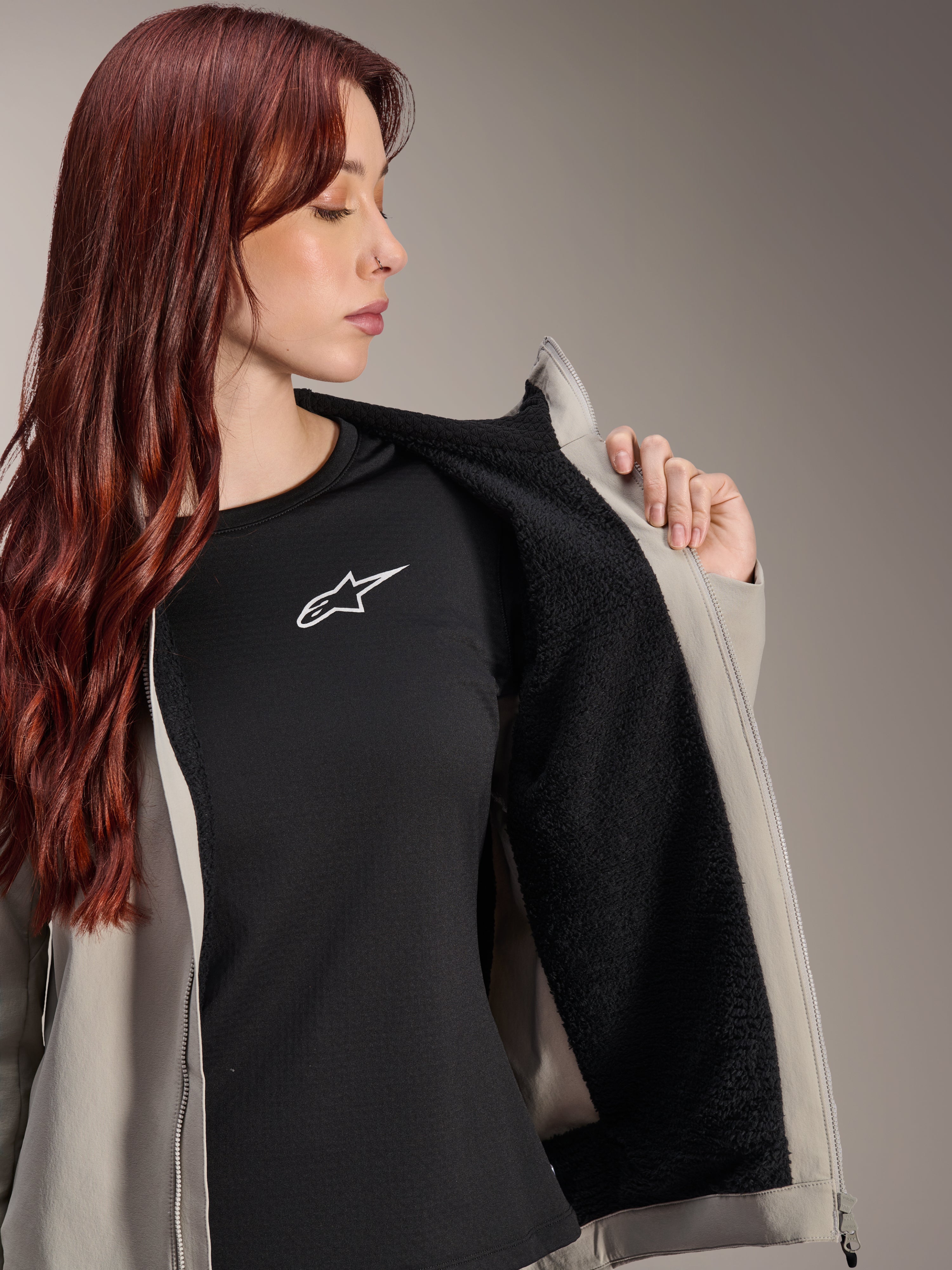 Femme portant la veste thermique Alpinestars Stella A-Dura en Titanium, présentant la doublure en polaire noire texturée, portée sur un t-shirt noir avec un logo étoile blanc, veste de VTT légère pour temps froid