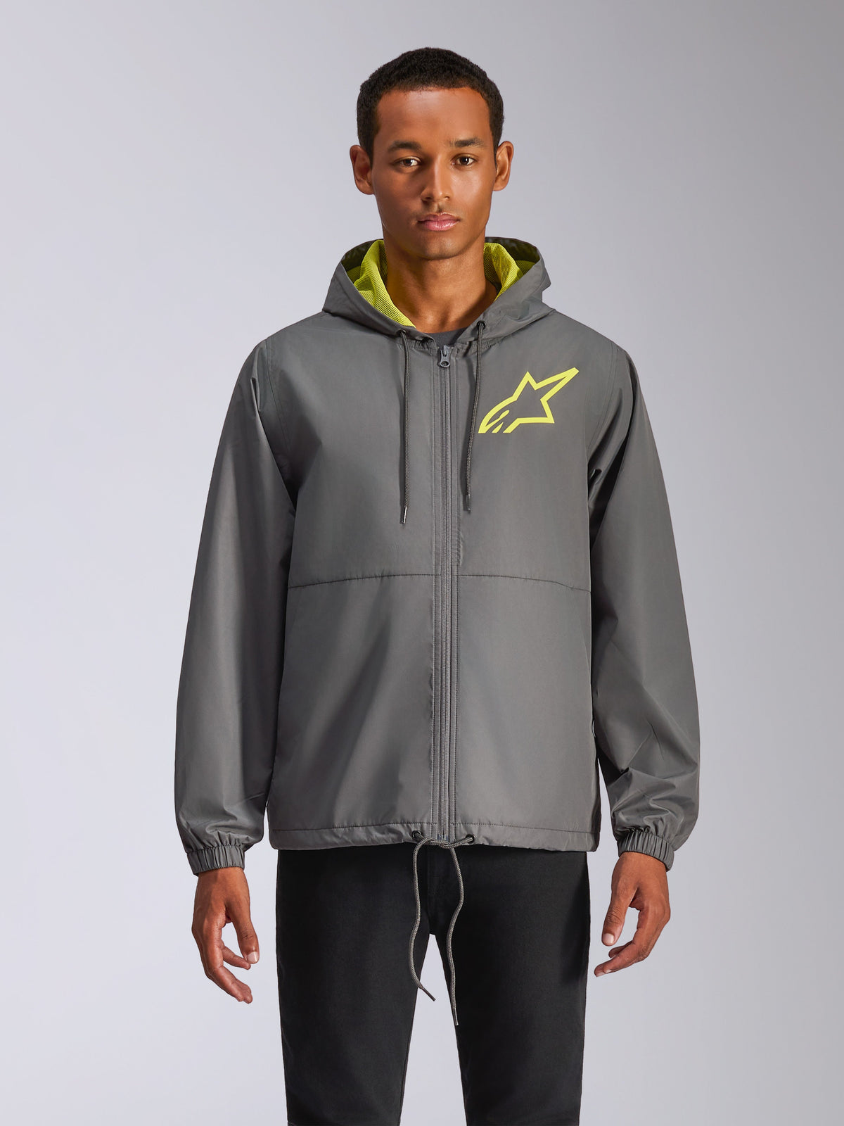 Alpinestars Speeder Chromium Windbreak Jacket, anthrazitgraue Windjacke mit Kapuze, neongelbes Stern-Logo, hellgrünes Kapuzenfutter, elastische Bündchen, verstellbare Kordelzüge, Frontreißverschluss, lässiger Motorsport-Stil