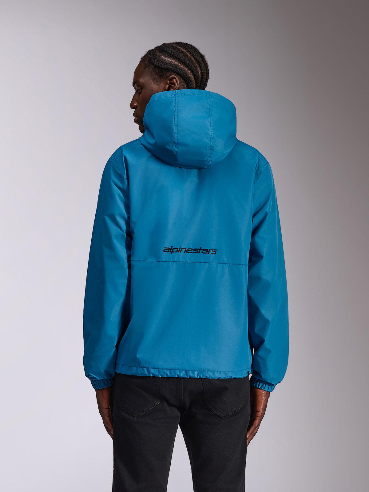 Alpinestars Speeder Chromium Windbreaker Jacket, blauw, achteraanzicht op model met zwart woordmerklogo op de rug, lichtgewicht windbreaker met capuchon en elastische manchetten, casual sportkleding.