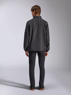 Veste Alpinestars Overhaul Racer, noir, vue de dos d'un homme portant la veste de pluie, tissu résistant à l'eau 2.5L, poignets élastiqués et capuche fixe, associée à un pantalon noir, vêtement d'extérieur décontracté inspiré du sport automobile