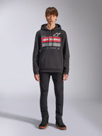 Alpinestars Harken hoodie, zwarte pullover hoodie, opvallende grafische print op de borst met rode strepen en de tekst 'Racing Ahead', wit Astars-logo, kangoeroezak, capuchon met trekkoord, casual motorsport-geïnspireerde streetwear, persoon draagt de hoodie met zwarte broek