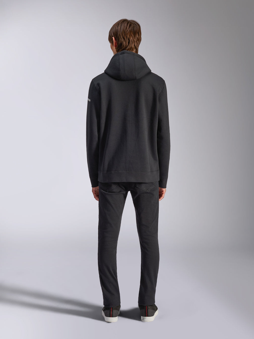 Alpinestars Frontal Hoodie, streetwear décontracté, noir, vue arrière d'un mannequin portant un sweat à capuche en polaire à enfiler, doté d'un ourlet et de poignets côtelés, petit logo wordmark blanc sur la manche, associé à un pantalon noir