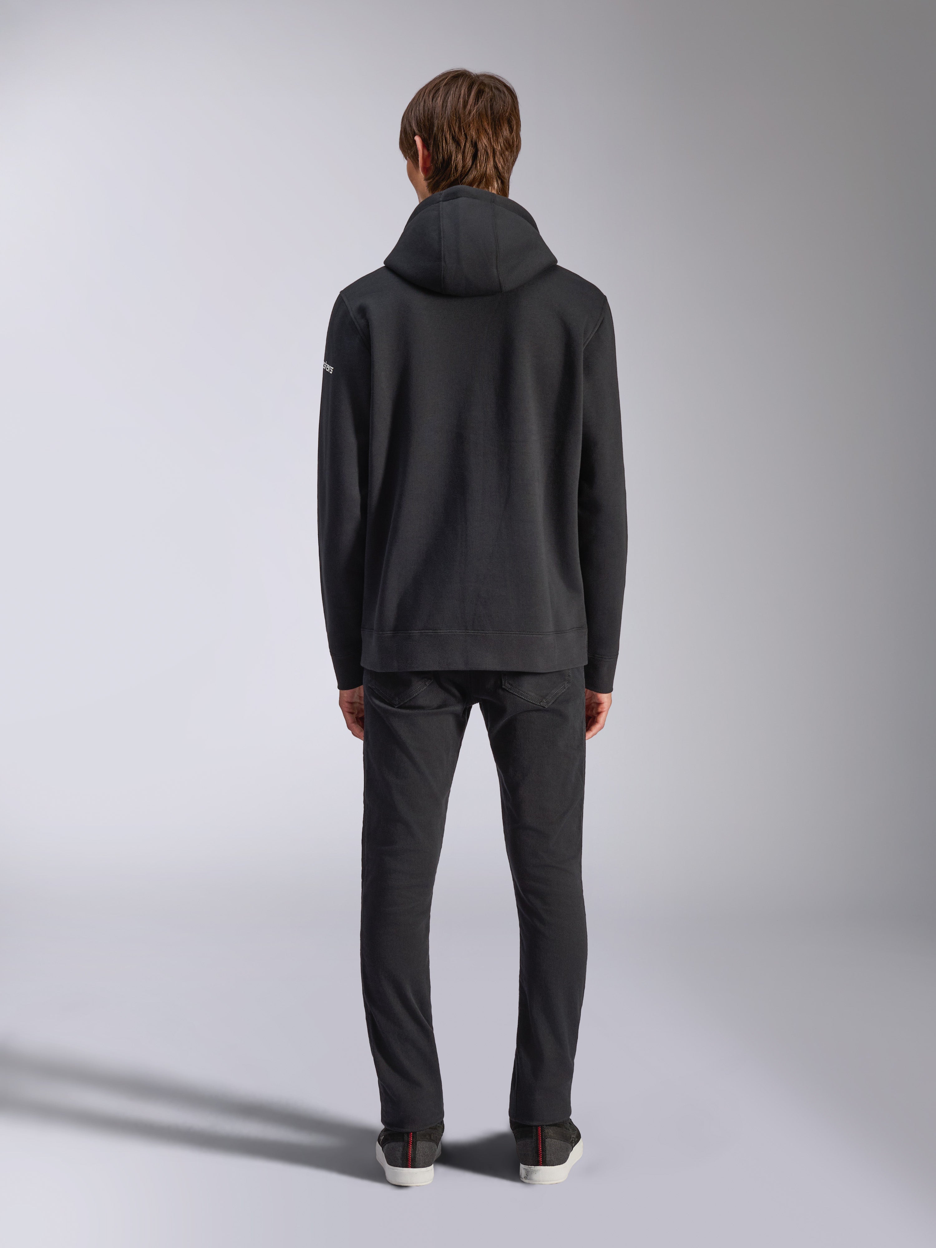 Alpinestars Frontal Hoodie, streetwear décontracté, noir, vue arrière d'un mannequin portant un sweat à capuche en polaire à enfiler, doté d'un ourlet et de poignets côtelés, petit logo wordmark blanc sur la manche, associé à un pantalon noir
