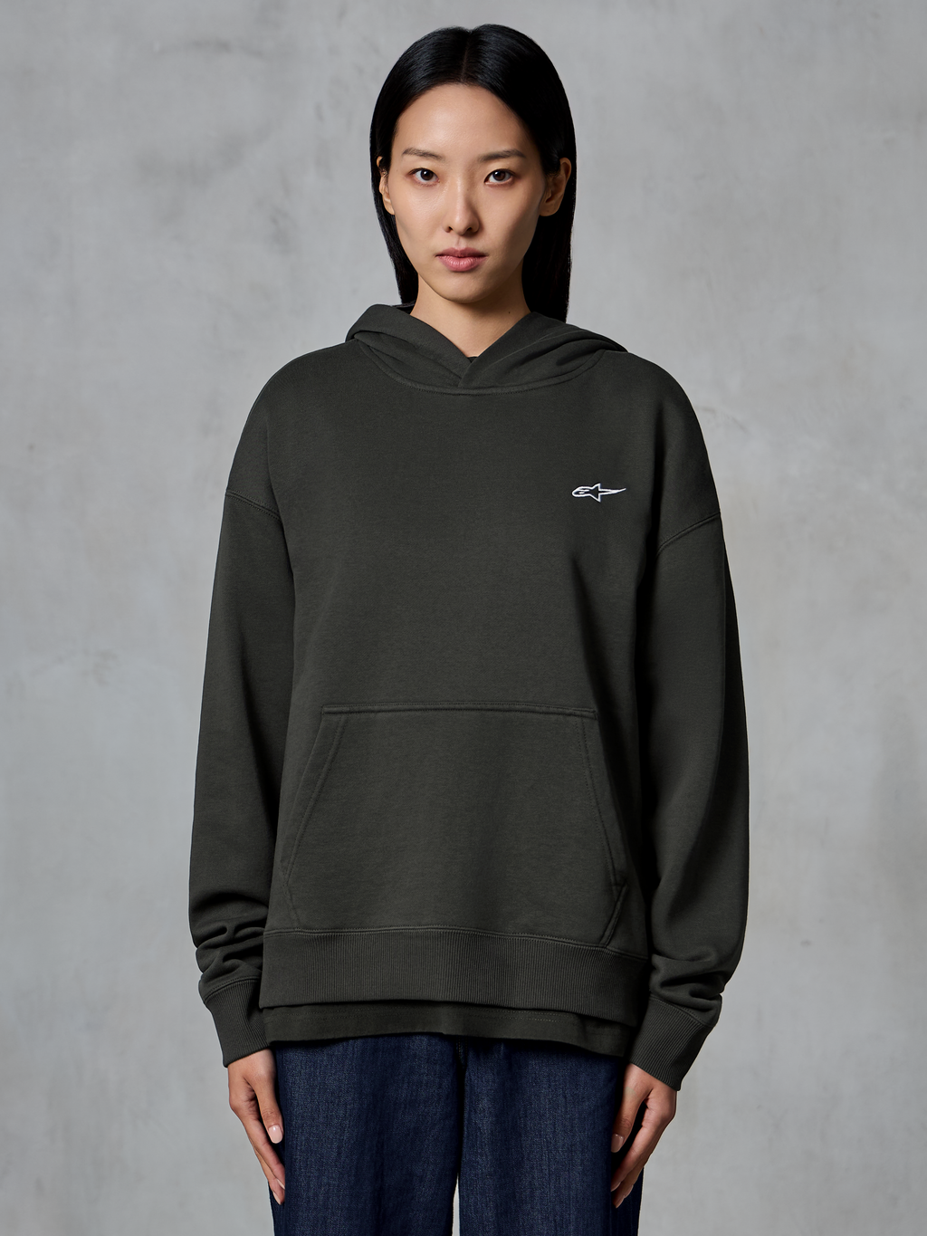 Alpinestars Essentials Ageless Hoodie, Off Black, von einem Model getragen, mit kleinem weißen Astars-Logo auf der Brust, Kängurutasche vorne, Stone-Wash-Finish, lässige Premium-Fleece-Streetwear