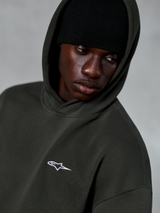 Alpinestars Essentials Ageless Hoodie, Off Black, close-up van een model dat een zwarte muts onder de capuchon draagt, voorzien van een klein wit sterlogo op de borst, casual streetwear geïnspireerd op de motorsport