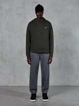 Model draagt Alpinestars Essentials Ageless Hoodie, casual streetwear, Off Black met klein wit logo op de borst, gecombineerd met grijze joggingbroek, zwarte beanie en zwarte sneakers, minimalistisch op motorsport geïnspireerd design