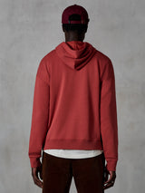 Alpinestars Essentials Ageless Hoodie, casual fleece hoodie, Brick rood, achteraanzicht van model in lifestyle kleding, voorzien van een strak ontwerp met geribbelde zoom en manchetten, gecombineerd met een bruine corduroy broek en een bordeauxrode pet