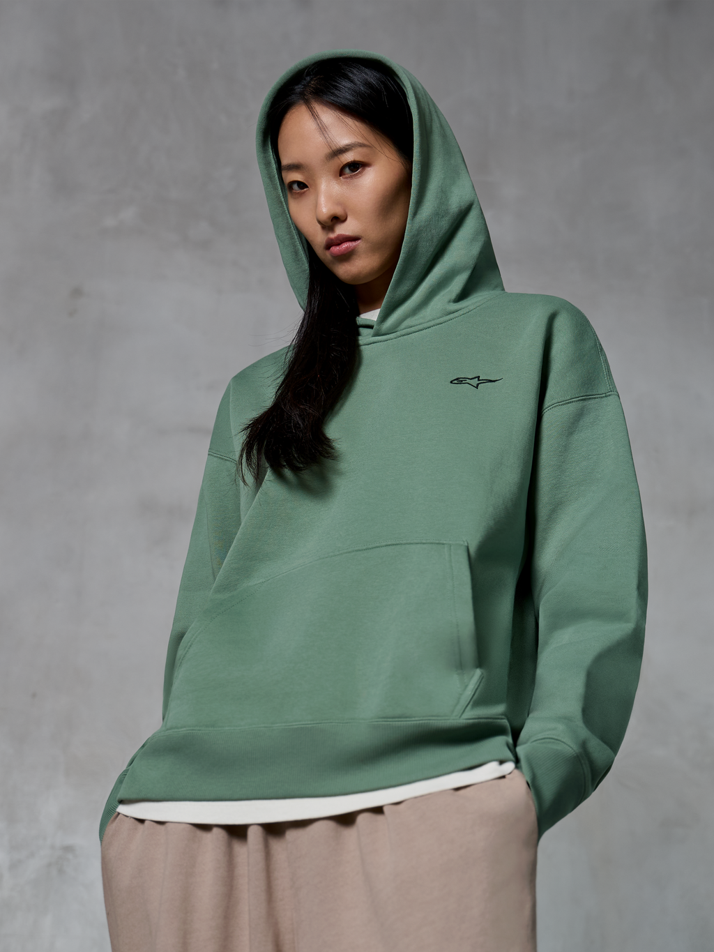 Alpinestars Essentials Ageless Hoodie, lässige Streetwear, Kaktusgrün mit kleinem schwarzem Logo, Hoodie mit aufgesetzter Kapuze, Kängurutasche vorne, Stone-Wash-Finish, kombiniert mit hellbeiger Hose