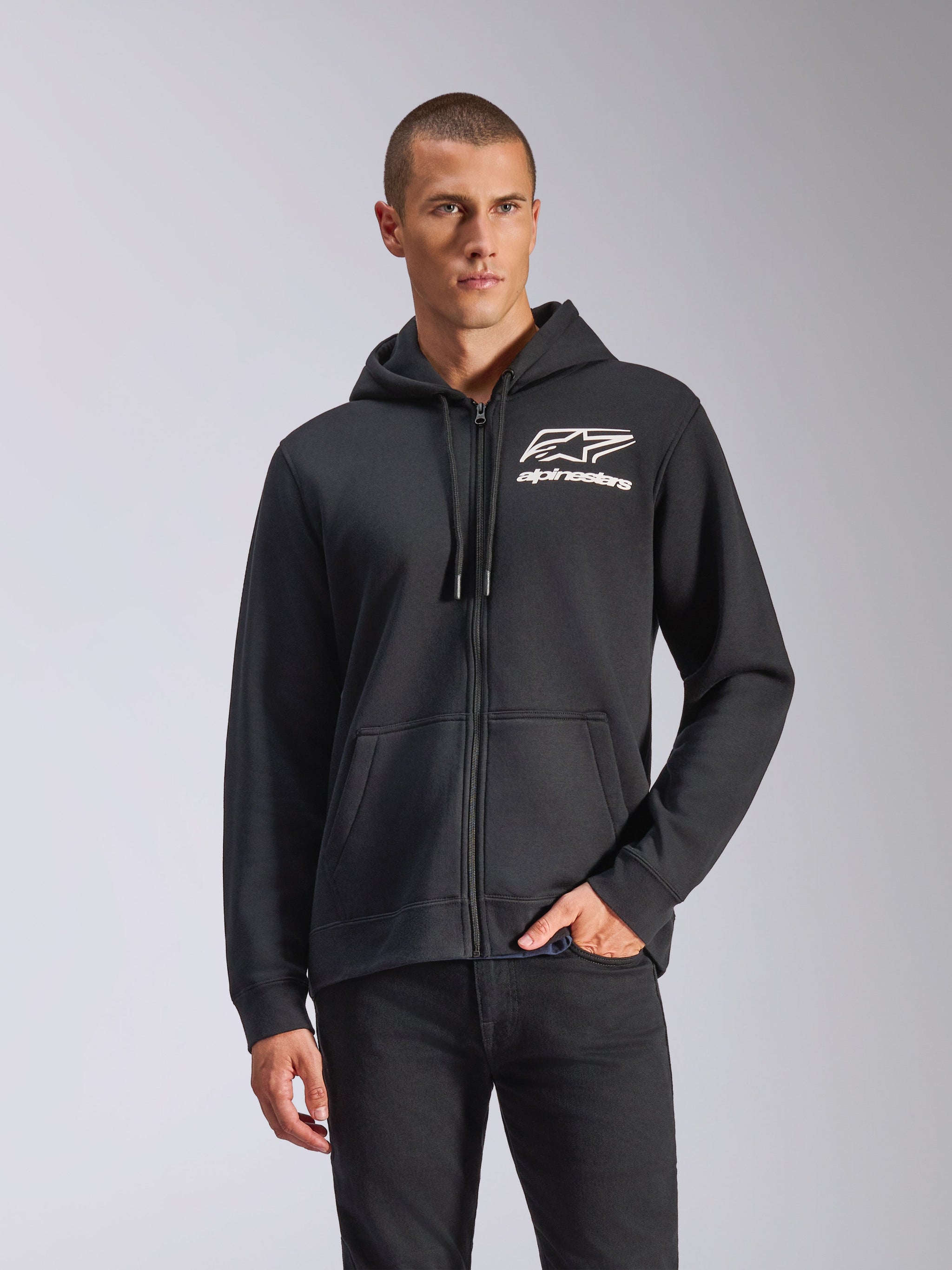 Alpinestars Formulation Hoodie, schwarze Kapuzenjacke mit Reißverschluss, weißes Alpinestars-Logo auf der Brust, Kapuze mit technischen Kordelzügen, von einem Mann getragen, lässige, vom Motorsport inspirierte Sportbekleidung