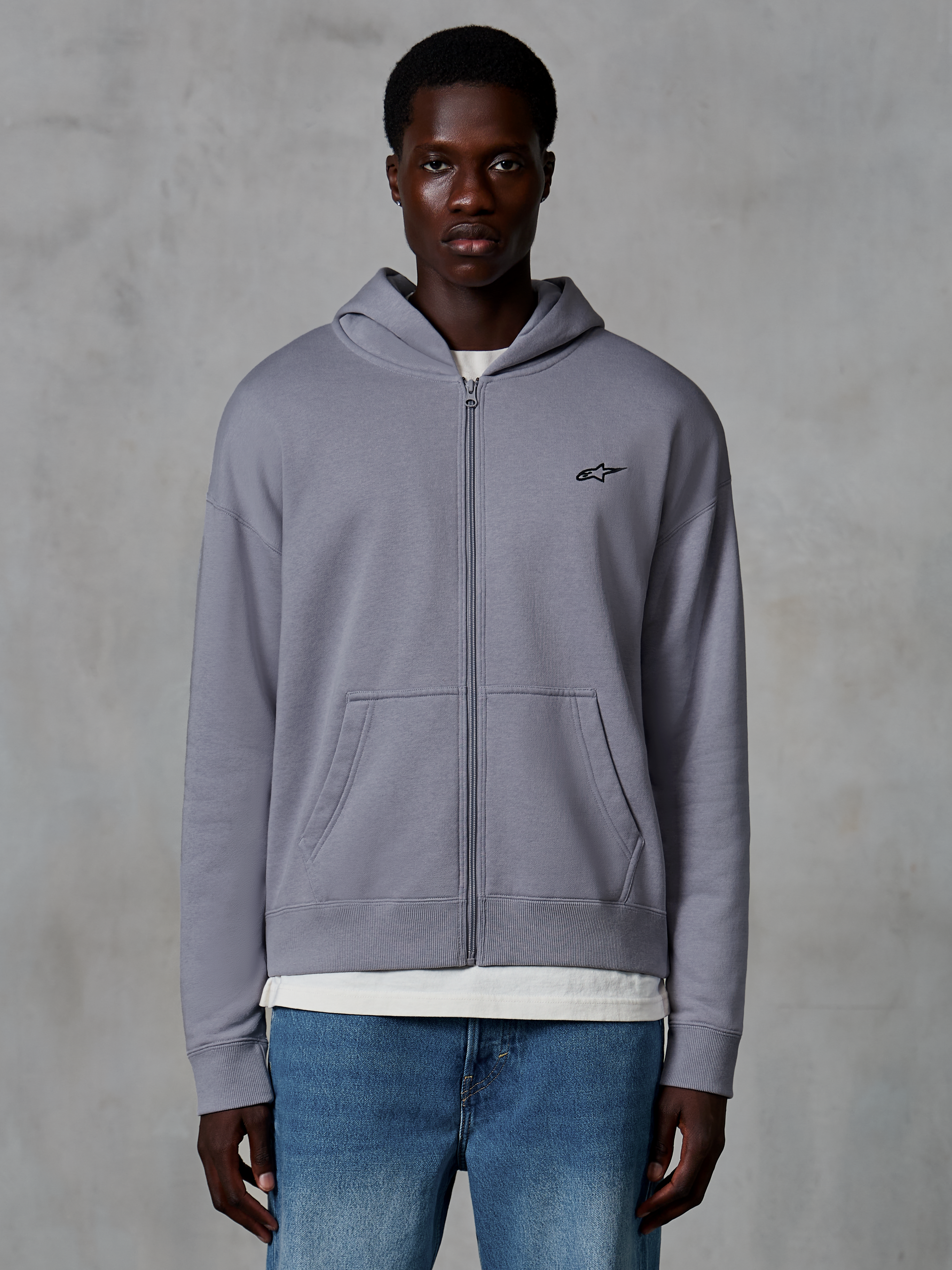Alpinestars Essentials Ageless Zip Hoodie, zilver, casual streetwear gedragen door model, fleece met volledige ritssluiting en klein zwart Astars-logo op de borst, kangoeroezakken, ontspannen pasvorm