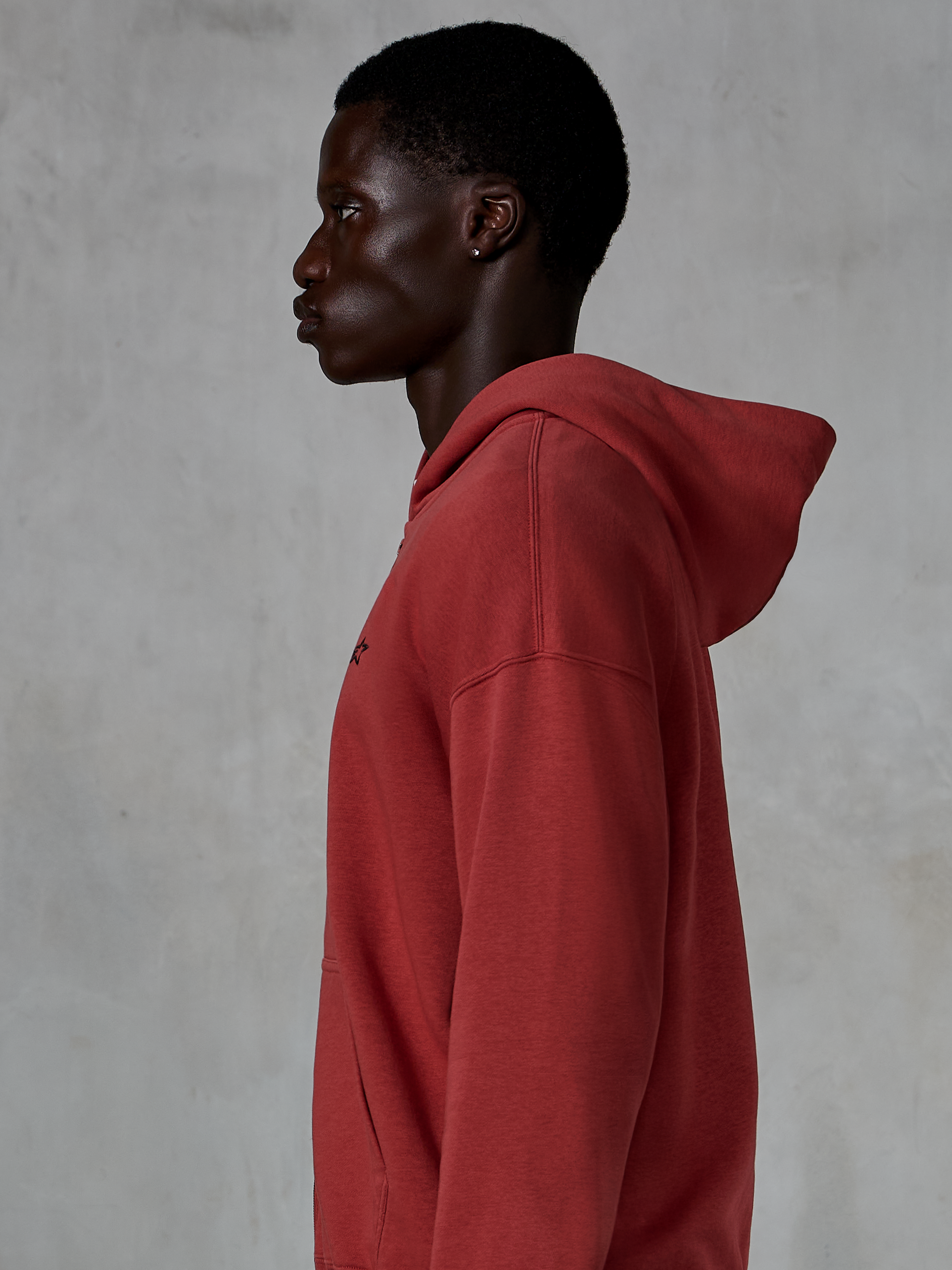 Alpinestars Essentials Ageless Zip Hoodie, Ziegelrot, Seitenprofilansicht eines Mannes in einem locker sitzenden Kapuzenpullover mit Reißverschluss, kleines schwarzes Stern-Logo auf der Brust, hochwertiges Stone-Washed-Fleece, lässige Motorsport-Streetwear