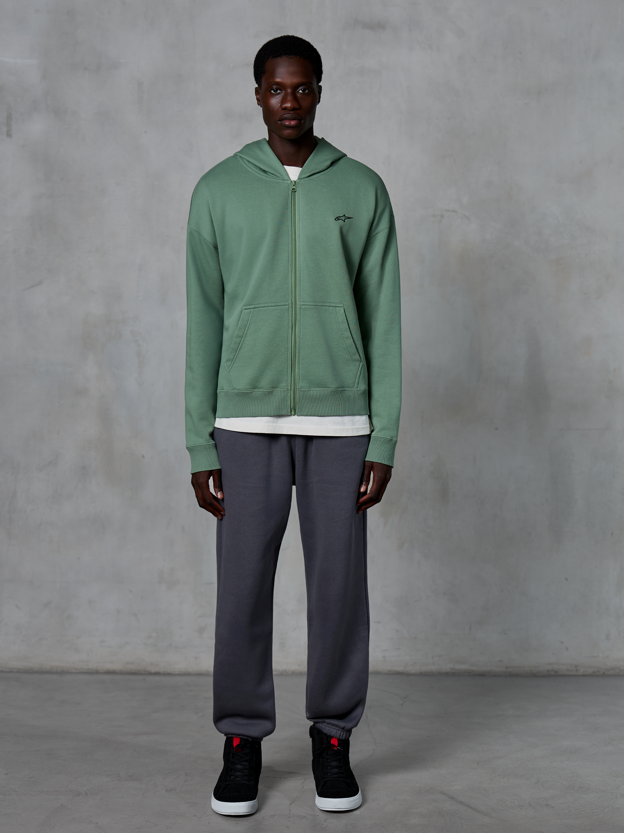 Alpinestars Essentials Ageless Zip Hoodie, Zip-up Hoodie, Cactus Green, worn by a model with dark grey joggers and black sneakers, featuring a small black Alpinestars logo on the chest, relaxed fit, casual streetwear.