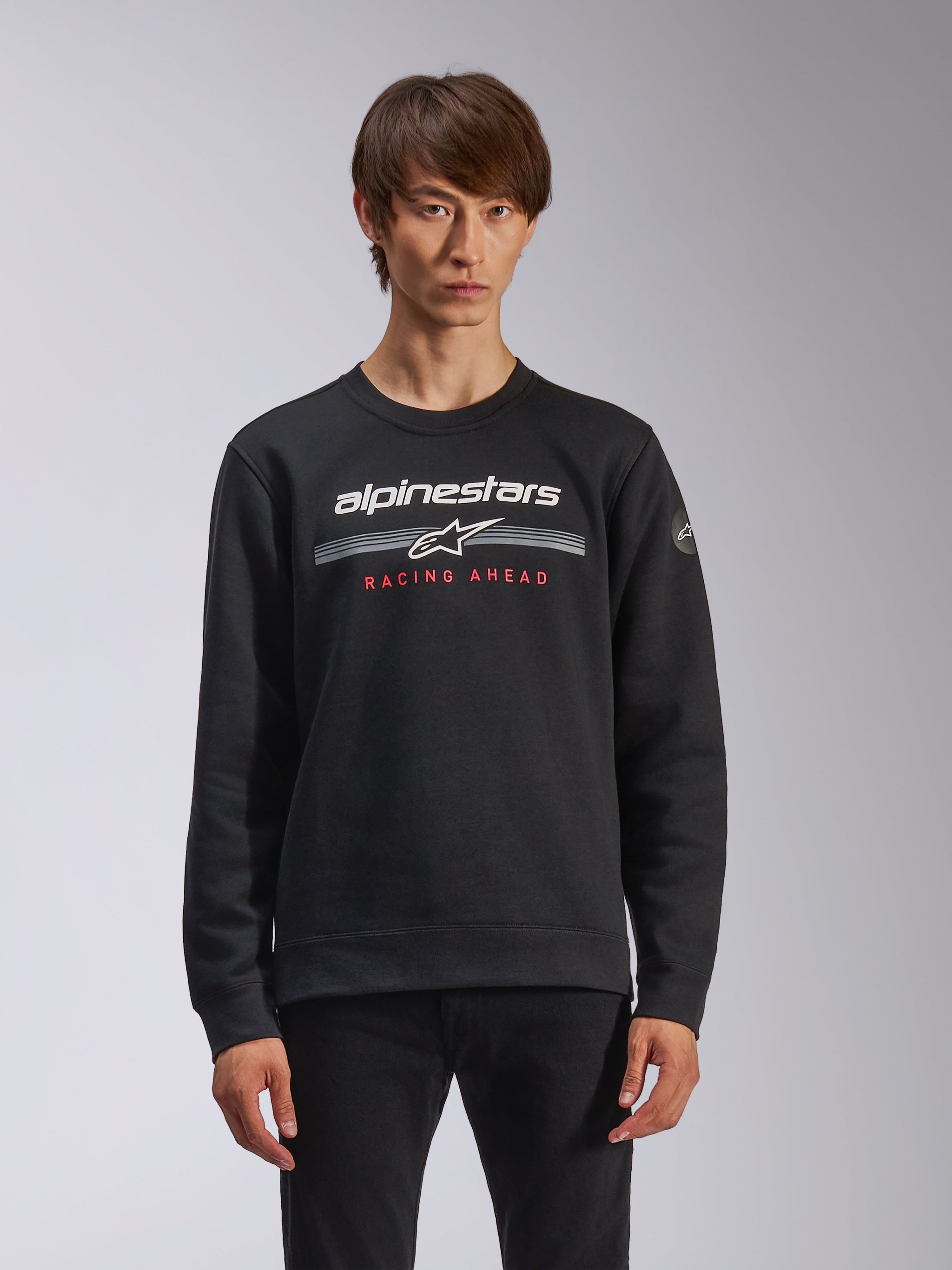 Alpinestars Bettern Crew, crewneck sweatshirt, zwart, met witte Alpinestars-branding, horizontale grijze strepen en rode 'RACING AHEAD' tekst, casual motorsport streetwear