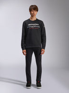 Alpinestars Bettern Crew, sweatshirt noir à col rond, logo Alpinestars blanc avec rayures grises horizontales et texte 'RACING AHEAD' rouge, style streetwear décontracté, porté par un mannequin avec pantalon noir et baskets