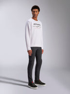 Alpinestars Bettern Crew, sweat-shirt blanc à col rond avec logo Alpinestars noir et texte rouge 'Racing Ahead', style streetwear décontracté inspiré du sport automobile, porté par un mannequin avec un pantalon sombre et des baskets noires