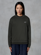 Alpinestars Essentials Ageless Crew, hochwertiges Rundhals-Sweatshirt, Off Black, mit einem kleinen weißen Alpinestars-Logo auf der Brust, lässiger Streetwear-Stil, getragen von einem Model mit dunkler Jeans