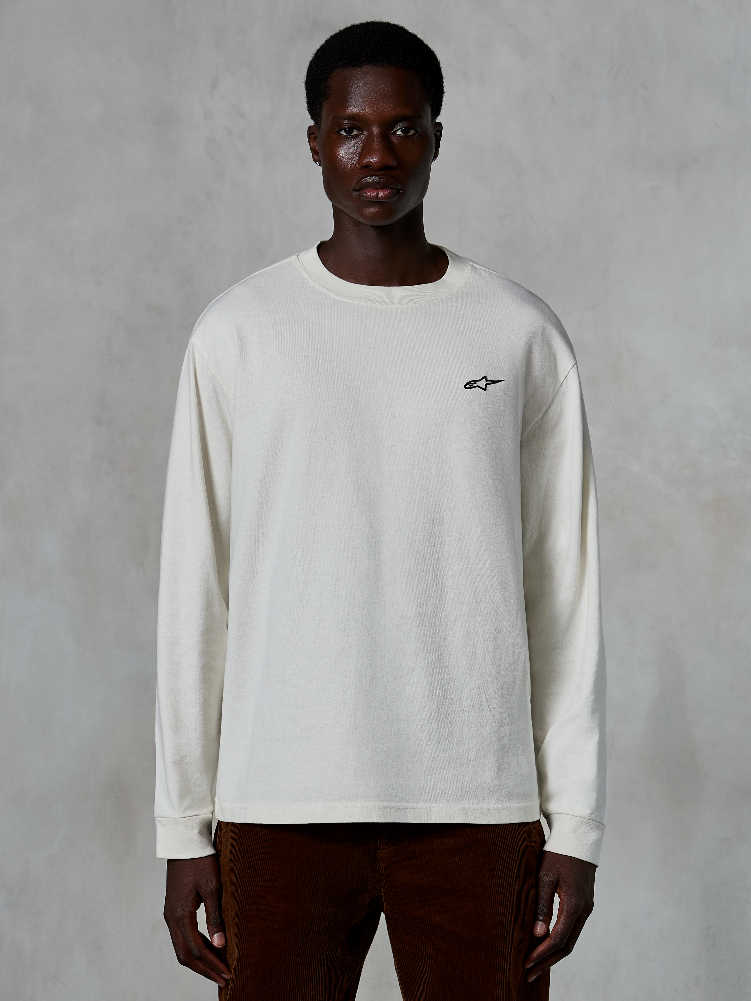 T-shirt à manches longues Alpinestars Essentials Ageless, blanc cassé, petit logo étoile noir sur la poitrine, streetwear décontracté, coupe décontractée, porté par un mannequin