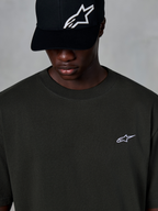 Alpinestars Essentials Ageless SS Tee, T-shirt met korte mouwen, Off Black, met een klein wit Alpinestars-logo op de borst, gedragen met een zwarte baseballcap met logo, casual motorsport streetwear stijl
