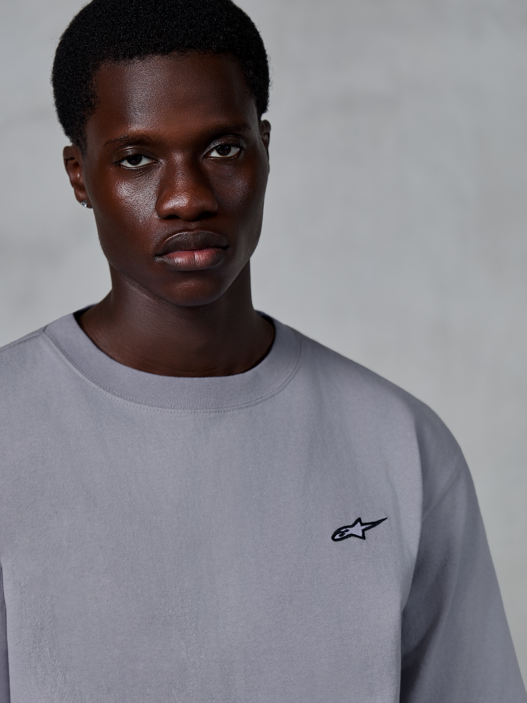 Alpinestars Essentials Ageless SS Tee, Kurzarm-T-Shirt, Silber, mit einem kleinen schwarzen Stern-Logo auf der Brust, getragen von einem Model, lässige Lifestyle-Streetwear