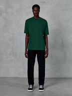 T-shirt Alpinestars Essentials Ageless SS, t-shirt à manches courtes, vert sapin, avec un logo noir discret sur la poitrine, porté par un mannequin avec un pantalon noir et des baskets, style streetwear décontracté avec une coupe décontractée