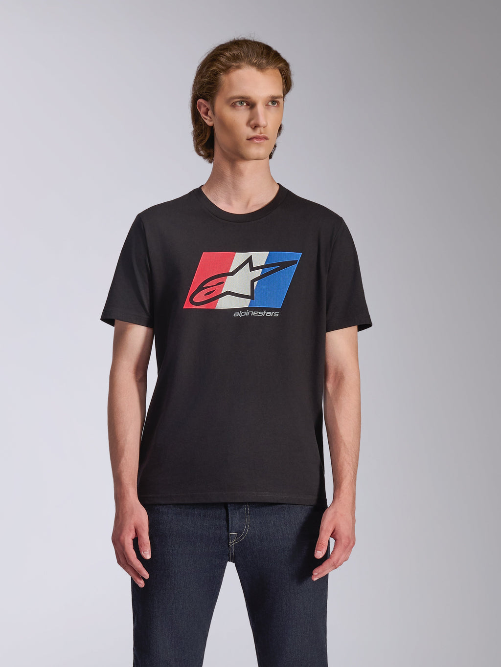 Alpinestars Global CSF Tee, T-shirt met korte mouwen, zwart, rood wit en blauw Ageless logo graphic, gedragen door mannelijk model met donkere jeans, casual motorsport streetwear