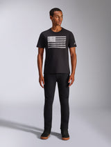 Alpinestars Waving CSF Tee, Kurzarm-T-Shirt, Schwarz, mit einer weißen Grafik im Distressed-Flaggen-Stil auf der Brust, getragen von einem Model mit schwarzer Hose und schwarzen High-Top-Sneakern, Casual Motorsport Streetwear