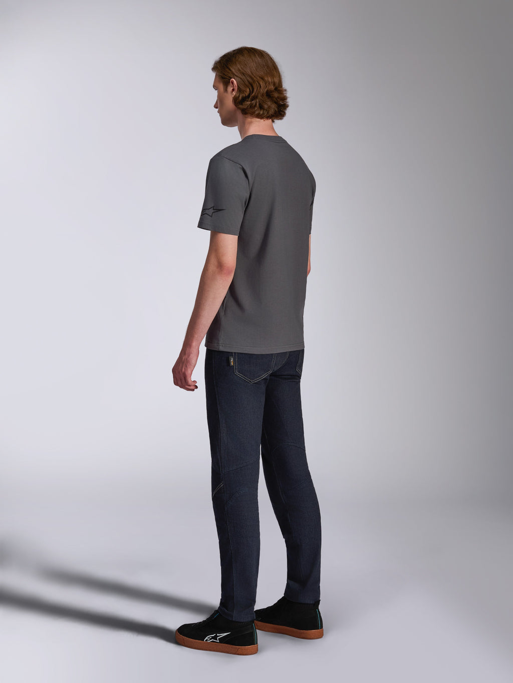 Alpinestars Waving CSF Tee, T-shirt met korte mouwen, Charcoal, achteraanzicht op model, klein zwart sterlogo op de mouw, gedragen met donkere denim jeans en zwarte sneakers, casual motorsport streetwear