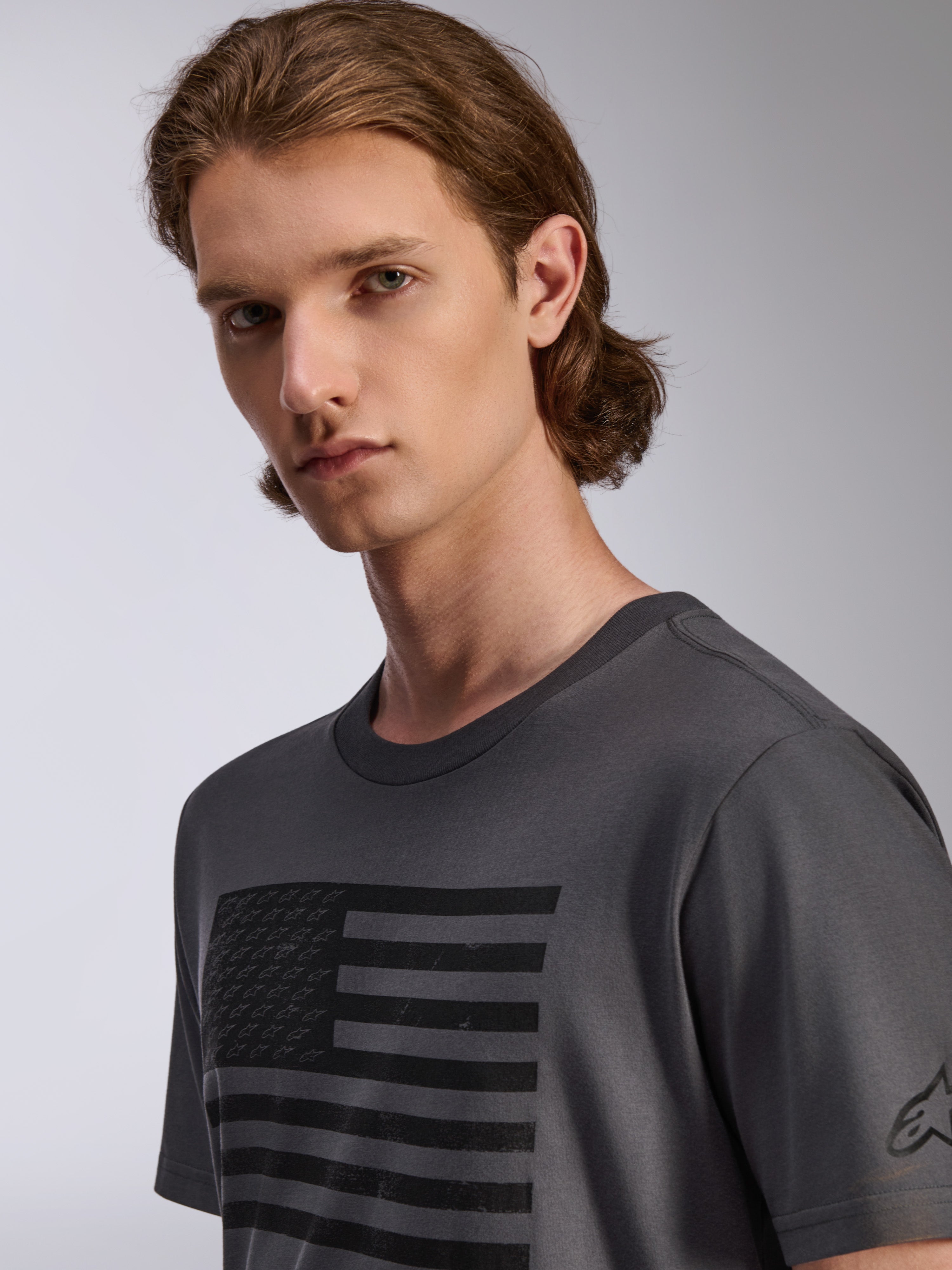 Alpinestars Waving CSF Tee, T-shirt met korte mouwen, charcoal, met een zwarte graphic van een versleten vlag met kleine sterlogo's, casual sportkleding voor heren, man draagt het shirt